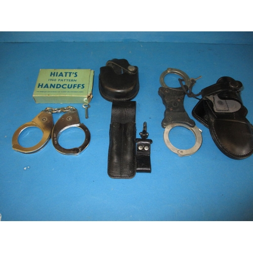 33 - Two pairs of police handcuffs, one set boxed dated 1960, both with leather holders and keys