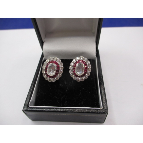 64 - A pair of 9ct white gold diamond and ruby earrings, having screw back fitting, the central stone mea... 