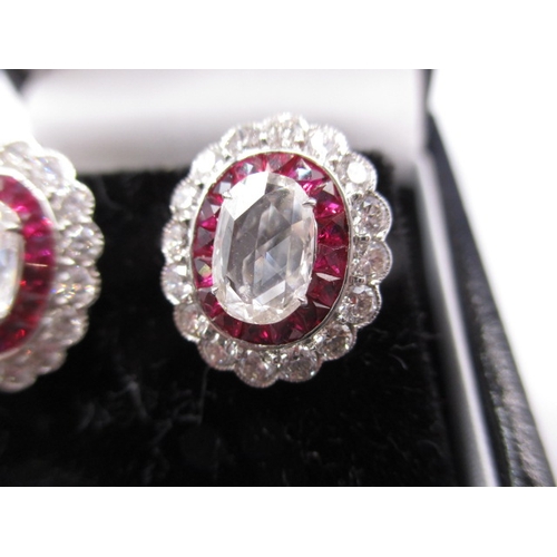 64 - A pair of 9ct white gold diamond and ruby earrings, having screw back fitting, the central stone mea... 