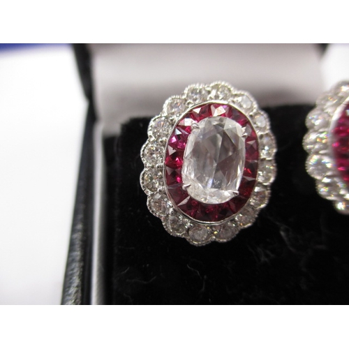 64 - A pair of 9ct white gold diamond and ruby earrings, having screw back fitting, the central stone mea... 