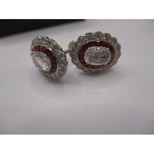 64 - A pair of 9ct white gold diamond and ruby earrings, having screw back fitting, the central stone mea... 