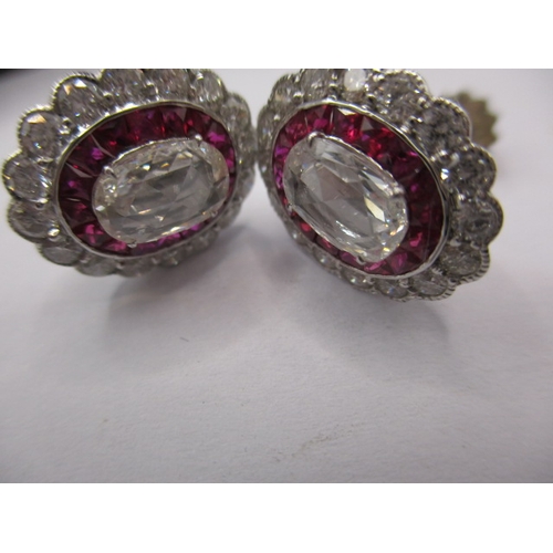 64 - A pair of 9ct white gold diamond and ruby earrings, having screw back fitting, the central stone mea... 