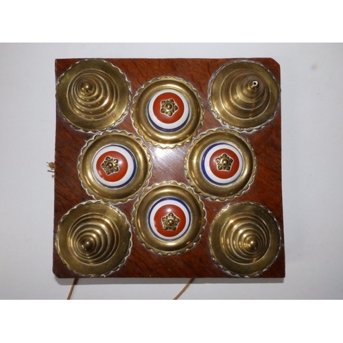 71 - Eight brass horse harness bosses mounted on a wood panel.