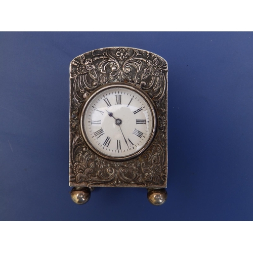 121 - An Asprey  miniature silver bedside clock, having embossed decoration, circular white enamel dial, o... 