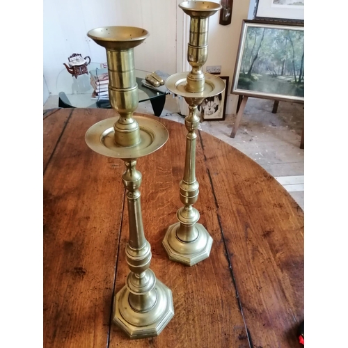 107 - A pair of tall antique brass candlesticks, having drip pans above slender stems to octagonal bases, ... 