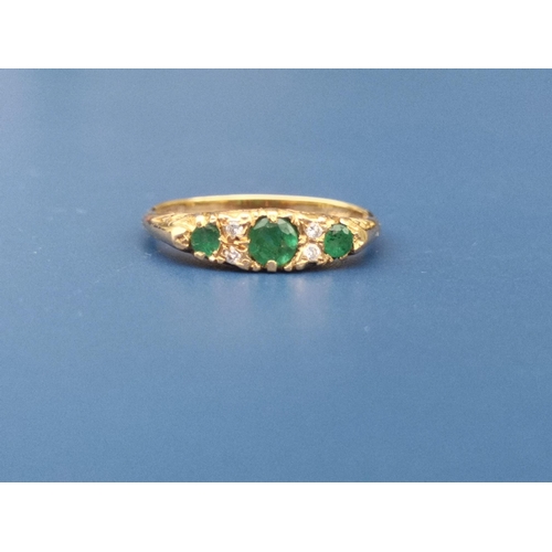 235 - An emerald & diamond  seven stone 18ct gold ring with scroll decorated shoulders, London marks.  Fin... 