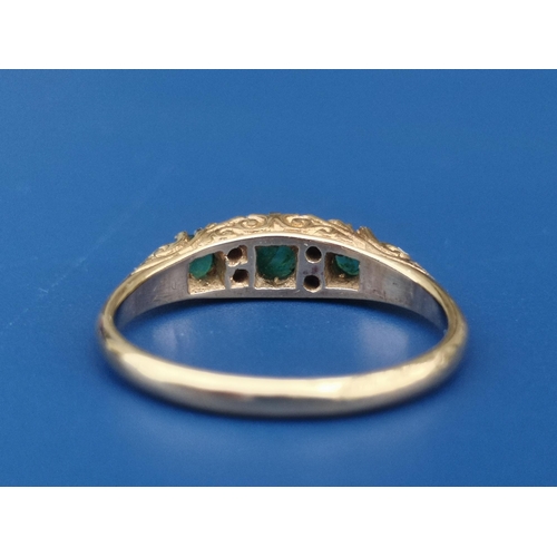 235 - An emerald & diamond  seven stone 18ct gold ring with scroll decorated shoulders, London marks.  Fin... 