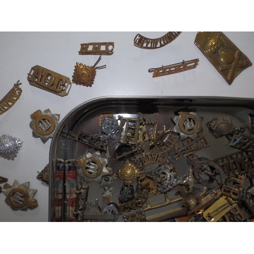 53 - A tin containing a large collection of military, badges, shoulder titles etc.