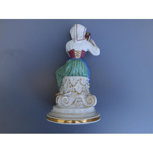 44 - A Meissen porcelain figure of a female tambourine player in folk costume, seated on an upturned Cori... 