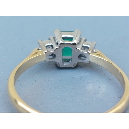 260 - A modern three stone emerald & diamond 18ct gold ring, the four-claw set rectangular cut emerald wei... 