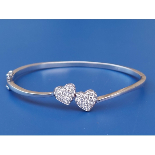 293 - A modern 18ct white gold bangle decorated with twin pave-set diamond hearts, maximum internal width ... 