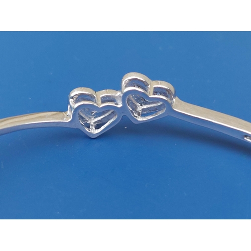 293 - A modern 18ct white gold bangle decorated with twin pave-set diamond hearts, maximum internal width ... 