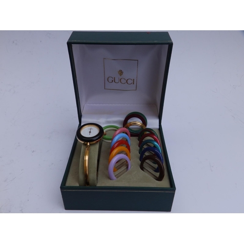 131 - A boxed ladies gold plated Gucci bangle wrist watch with 15 interchangeable plastic bezels,