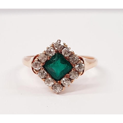 114 - AN EMERALD AND DIAMOND CLUSTER RING, with central emerald set at an angle, surrounded by a frame of ... 