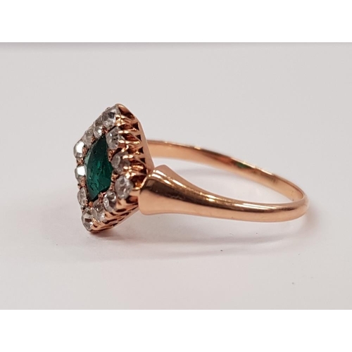 114 - AN EMERALD AND DIAMOND CLUSTER RING, with central emerald set at an angle, surrounded by a frame of ... 