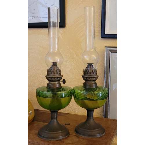 238 - A PAIR OF PAROFIN LAMPS, with green glass reservoir and brass column and fitting, clear glass chimne... 