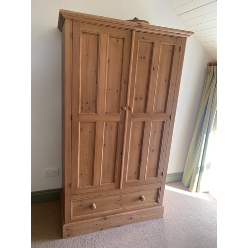 200 - A COUNTRY PINE TWO DOOR WARDROBE, with one drawer beneath, flared cornice, panelled doors, on platfo... 