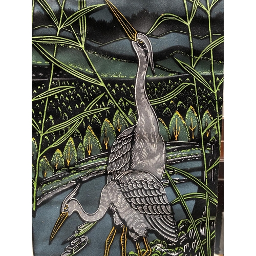 197 - A PAINTED WALL HANGING, depicting two herons in a riverside scene, surrounded by cattail plants. Fin... 