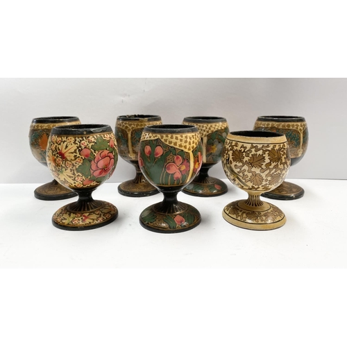 211 - A SET OF SEVEN HARDWOOD CARVED PAINTED EGG CUPS, numbered to base, along with a wooden painted Russi... 