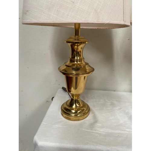 135 - A PAIR OF HEAVY BRASS LAMPS, with shaped polished brass body on circular platform base, with cream l... 