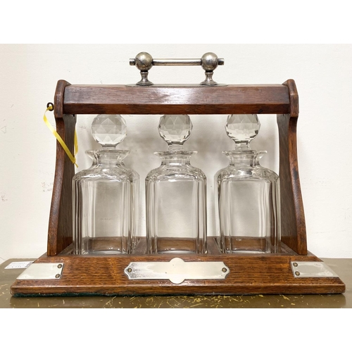 45 - AN ANTIQUE THREE BOTTLE TANTULUS, with three cut glass decanters/carafes, within oak frame with silv... 