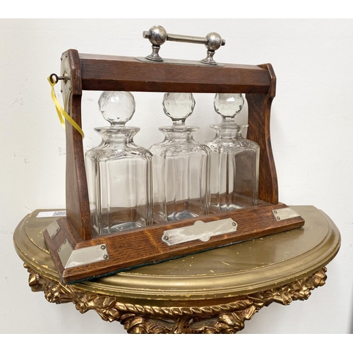 45 - AN ANTIQUE THREE BOTTLE TANTULUS, with three cut glass decanters/carafes, within oak frame with silv... 