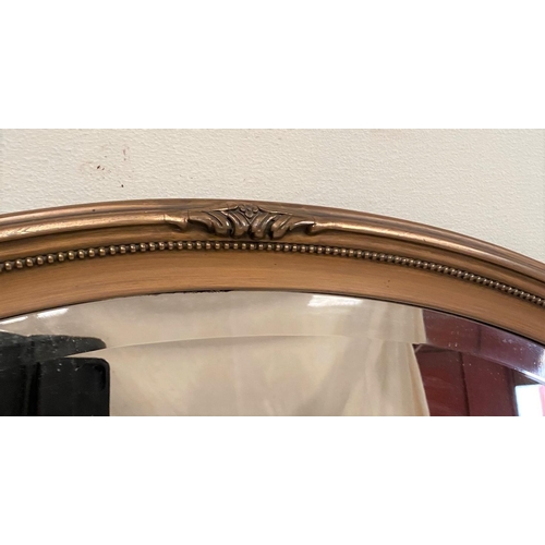 75 - AN OVAL GILT OVERMANTLE MIRROR, decorated with beading and scroll details to frame, with bevelled gl... 