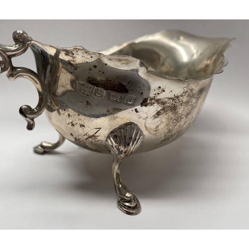 73 - A SILVER SAUCE BOAT, with shaped edge, double scroll handle, standing on three hoof feet. Maker S Bl... 