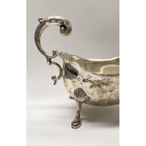 73 - A SILVER SAUCE BOAT, with shaped edge, double scroll handle, standing on three hoof feet. Maker S Bl... 