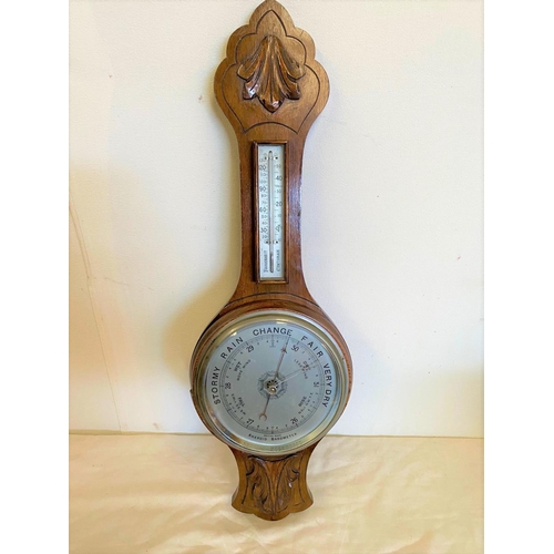 121 - AN OAK CASED ANEROID BAROMETER, British made. With carved leaf detail to the top, a silvered dial sh... 