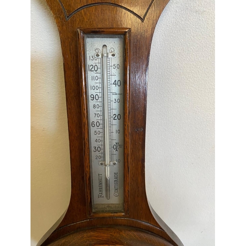 121 - AN OAK CASED ANEROID BAROMETER, British made. With carved leaf detail to the top, a silvered dial sh... 