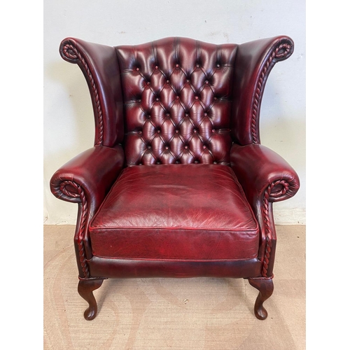 18 - A VERY GOOD QUALITY CHESTERFIELD STYLE BUTTONED WING BACK ARM CHAIR, the Ox-Blood coloured chair wit... 