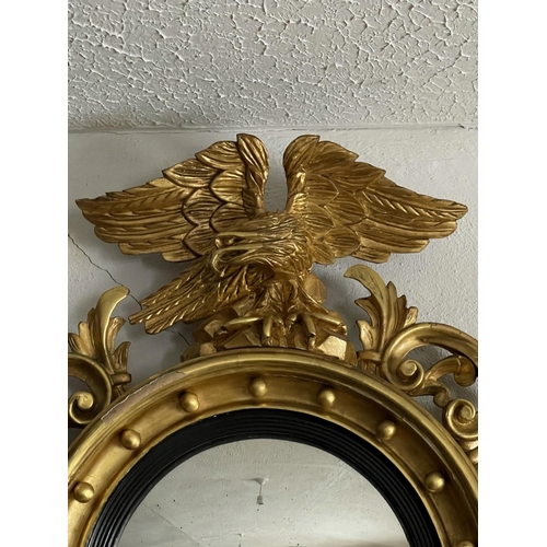 22 - AN ANTIQUE CARVED GIT WOOD CONVEX WALL MIRROR, with large carved eagle mount with its wings out-spre... 