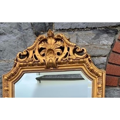 24 - A GILT ORNATE OVERMANTLE MIRROR, with bevelled glass in decorative frame with Neoclassical style car... 