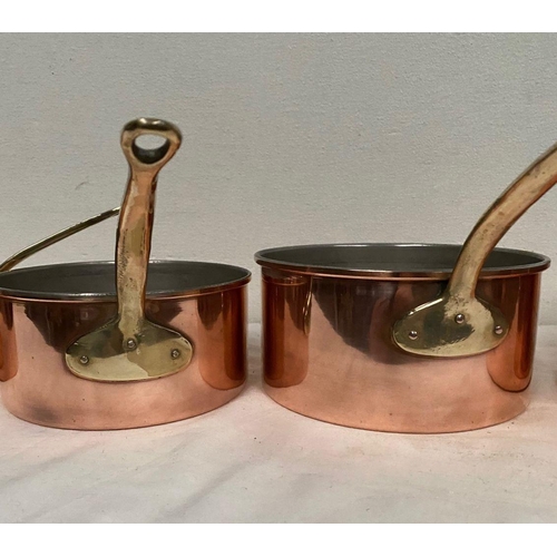 254 - A SET OF FIVE COPPER SAUCEPANS, with brass handles, in good condition.