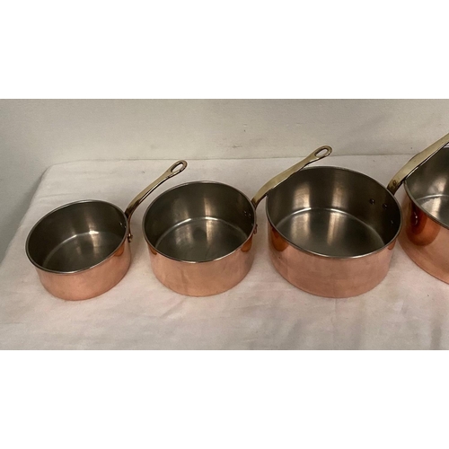 254 - A SET OF FIVE COPPER SAUCEPANS, with brass handles, in good condition.