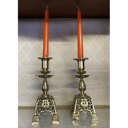 27 - A PAIR OF ORNATE BRASS CANDLESTICKS, with turned supports on square platform base with scrolling flo... 