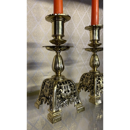 27 - A PAIR OF ORNATE BRASS CANDLESTICKS, with turned supports on square platform base with scrolling flo... 