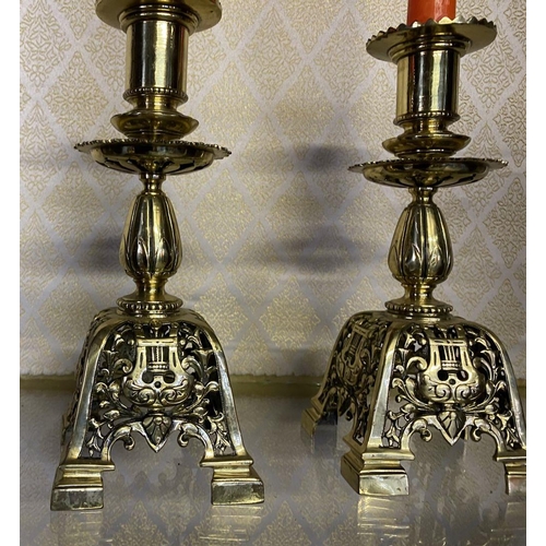 27 - A PAIR OF ORNATE BRASS CANDLESTICKS, with turned supports on square platform base with scrolling flo... 