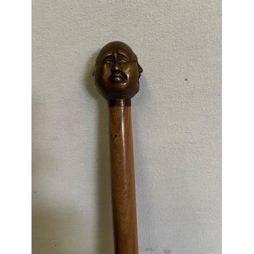 303 - AN ANTIQUE WALKING STICK WITH CARVING TO HANDLE, intricate carving of multiple faces to top, brass b... 