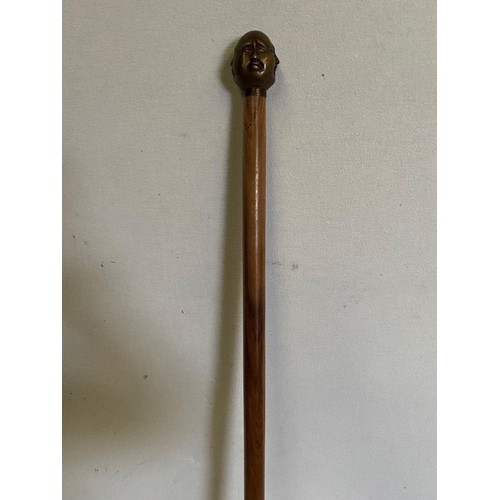 303 - AN ANTIQUE WALKING STICK WITH CARVING TO HANDLE, intricate carving of multiple faces to top, brass b... 