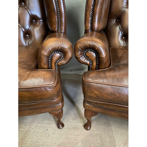 31 - A PAIR OF TAN LEATHER CHESTERFIELD WINGBACK ARMCHAIRS, stud upholstered with button back, scrolling ... 