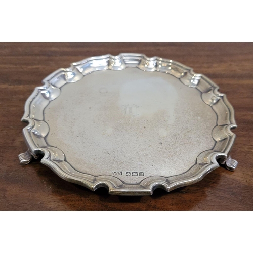 61 - AN EARLY 20TH CENTURY SOLID SILVER SALVER DISH, with a scalloped rim raised on a tripod of scrolling... 