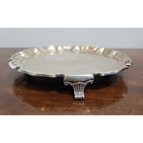 61 - AN EARLY 20TH CENTURY SOLID SILVER SALVER DISH, with a scalloped rim raised on a tripod of scrolling... 