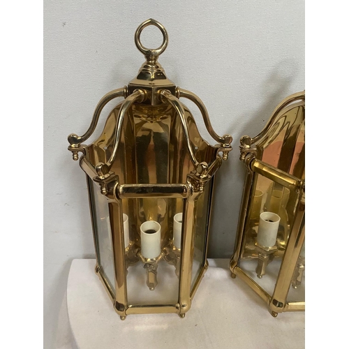 27 - A VERY GOOD QUALITY TRIO OF POLISHED BRASS WALL LANTERN LIGHTS, each with a triple bulb head the bac... 