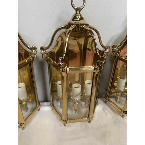 27 - A VERY GOOD QUALITY TRIO OF POLISHED BRASS WALL LANTERN LIGHTS, each with a triple bulb head the bac... 