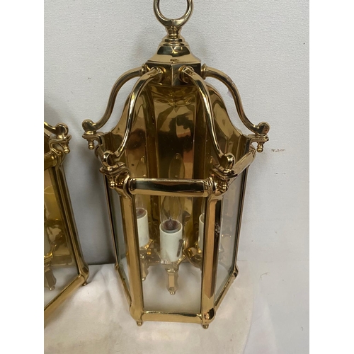 27 - A VERY GOOD QUALITY TRIO OF POLISHED BRASS WALL LANTERN LIGHTS, each with a triple bulb head the bac... 