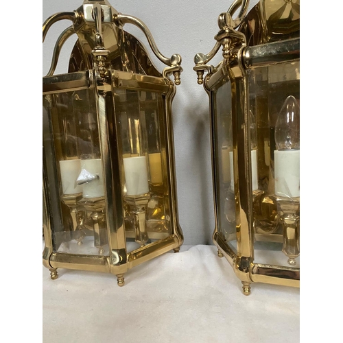 27 - A VERY GOOD QUALITY TRIO OF POLISHED BRASS WALL LANTERN LIGHTS, each with a triple bulb head the bac... 