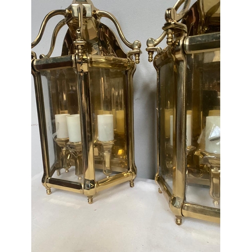 27 - A VERY GOOD QUALITY TRIO OF POLISHED BRASS WALL LANTERN LIGHTS, each with a triple bulb head the bac... 