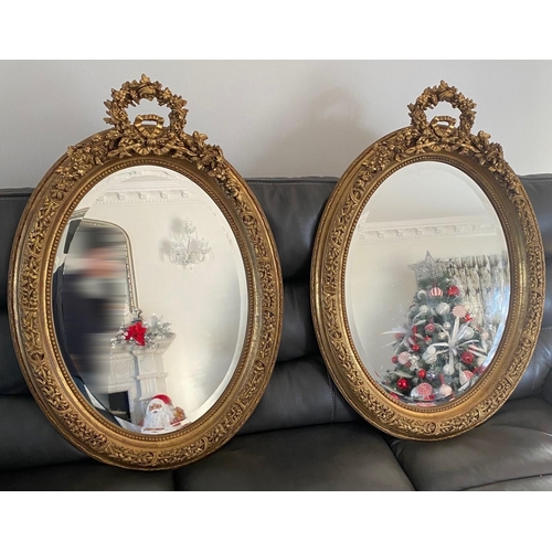 77 - A VERY FINE PAIR OF GILT OVAL SHAPED WALL MIRRORS, the mirrors with bevelled edge, the frames decora... 